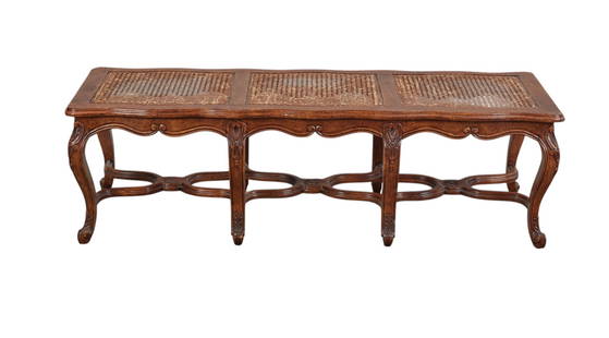 A Louis XV-style walnut caned bench: A Louis XV-style walnut caned benchThe rectangular cane seat divided into three panels within a moulded frame, above a shaped and carved apron, on eight cabriole legs with foliate carved knees, joined