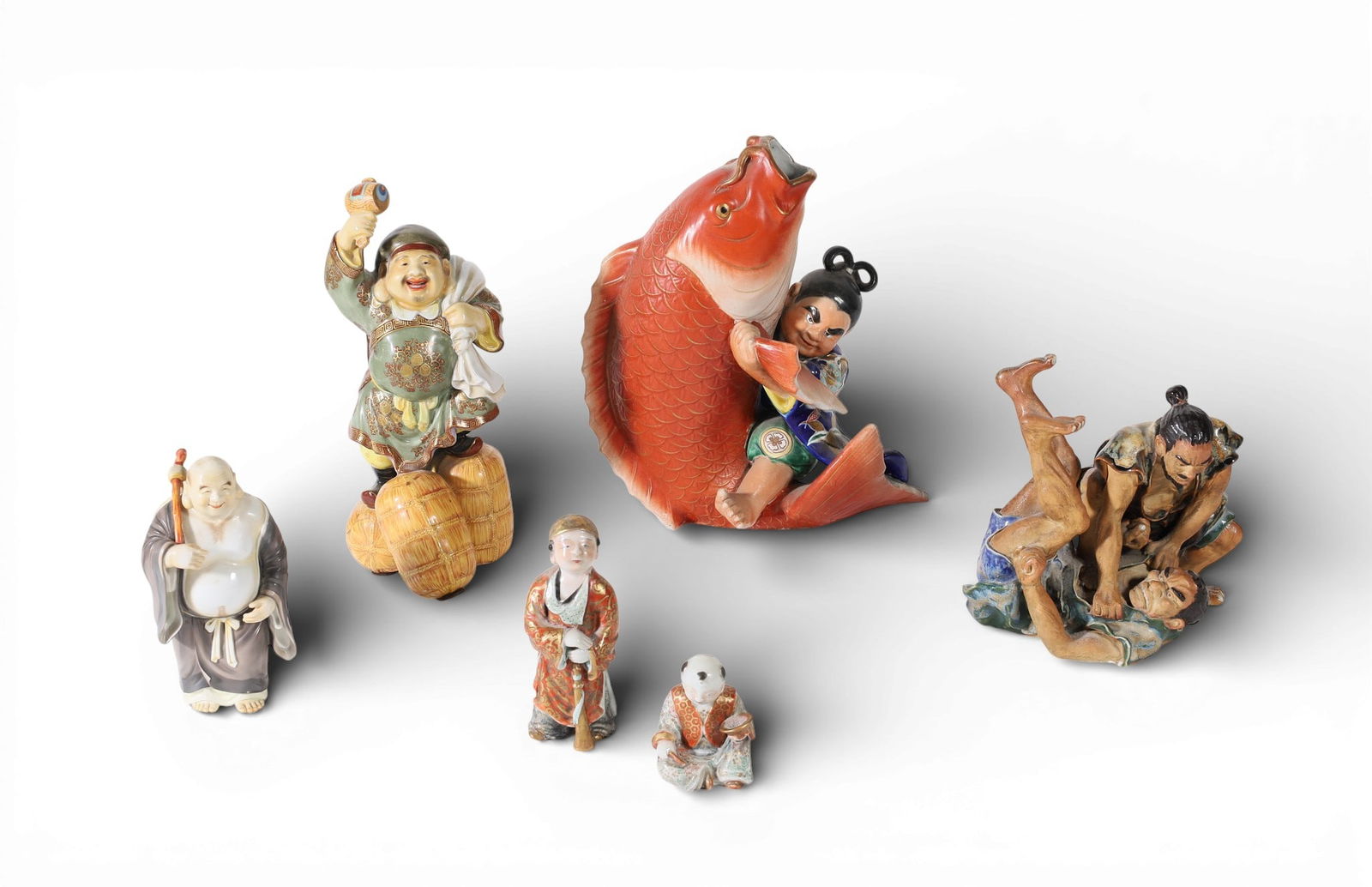 A group of six Japanese polychrome glazed ceramic figures and figural groups: A group of six Japanese polychrome glazed ceramic figures and figural groupsComprising a figure of Daikoku, the Laughing Buddha with red painted characters to underside, a Kutani koi fish and fisherma