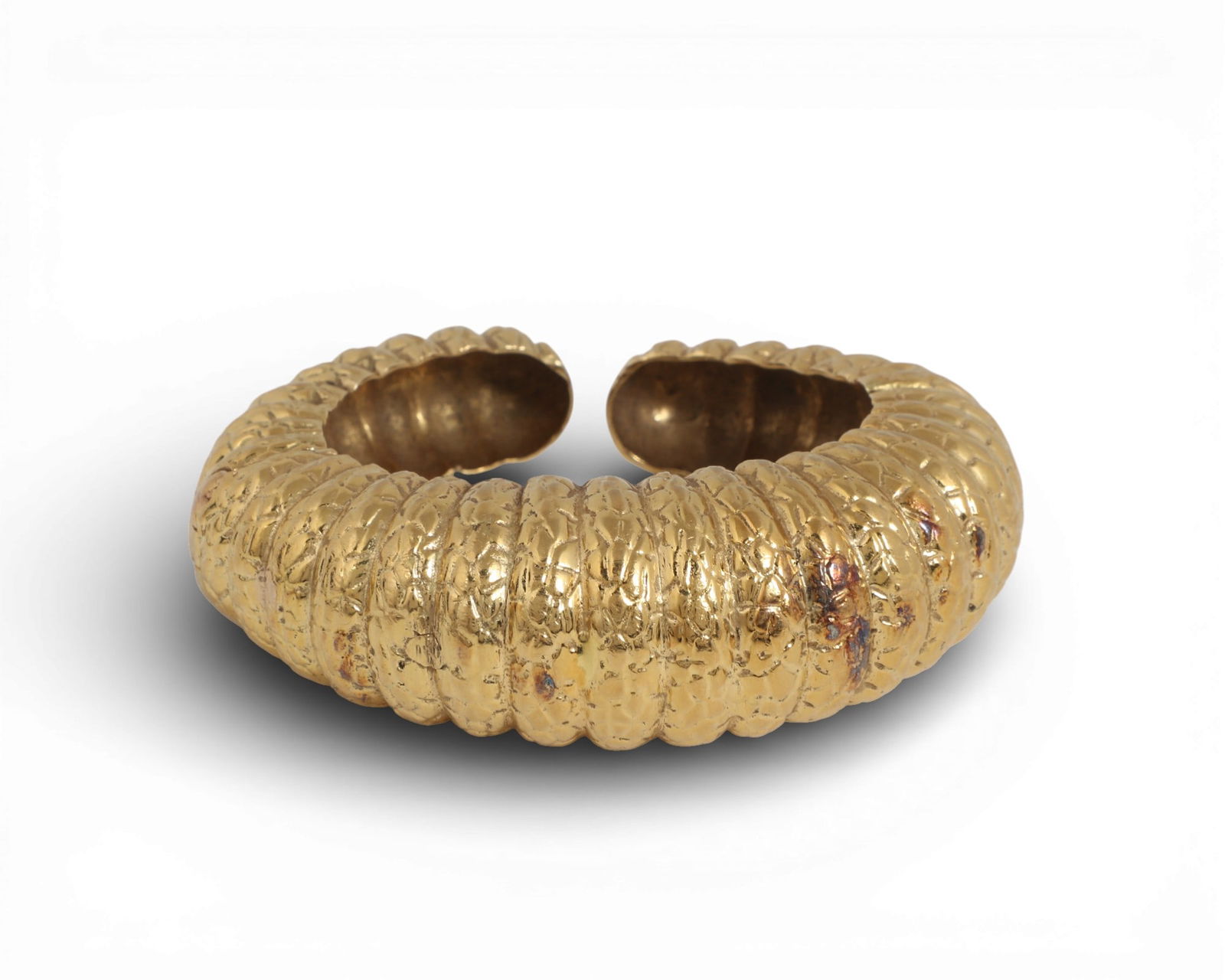 An 18K yellow gold bangle bracelet: An 18K yellow gold bangle braceletFluted hinged bangle with geometric patterns incised.inside diameter measures approximately 2.0 x 1.75in (5 x 4.5cm), width 14.5mm to 24mm; gross weight approximately