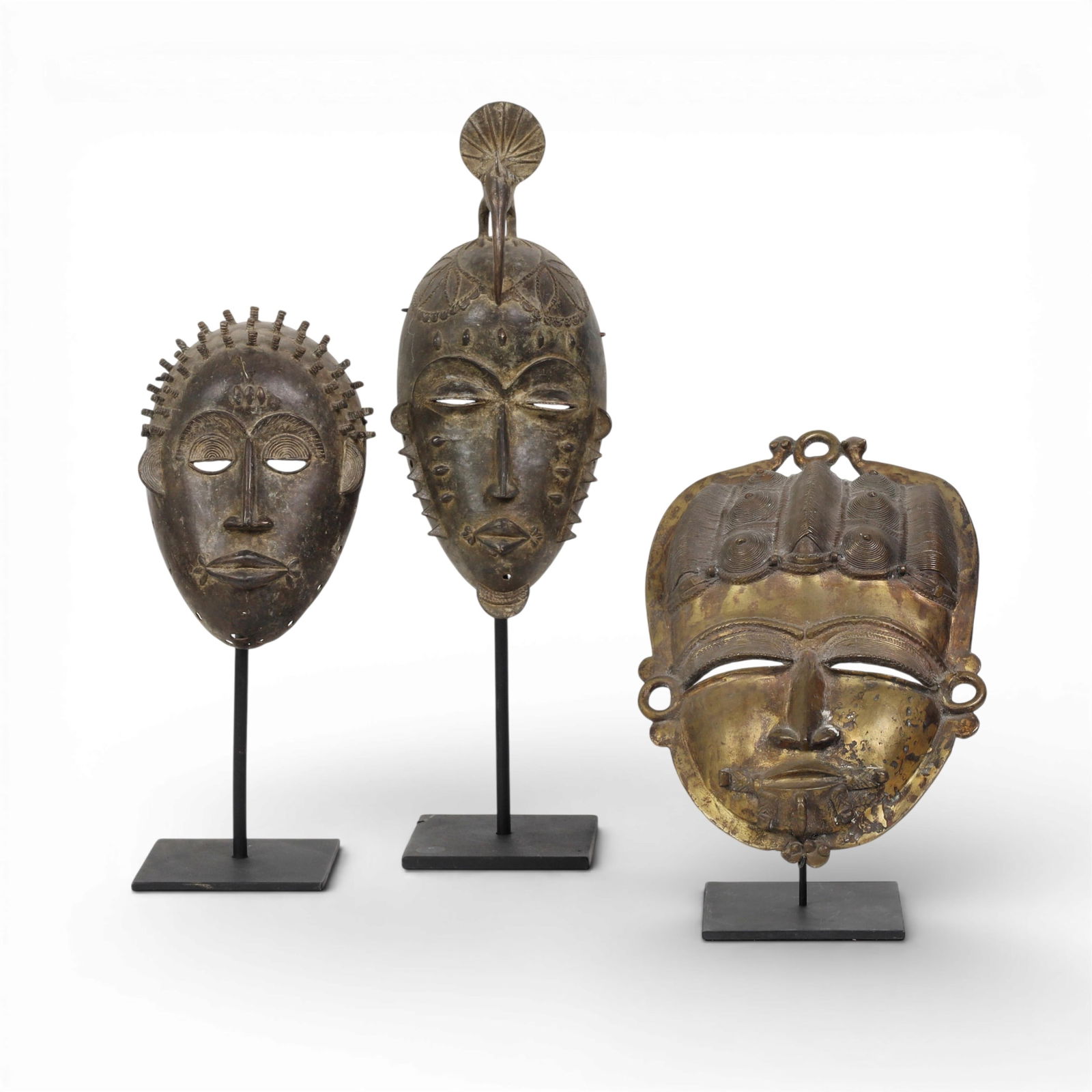 A group of three African metal masks on stands (1 of 4)