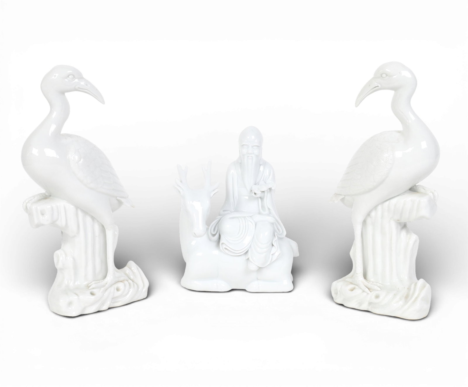 Three Chinese dehua or white glazed porcelain figures: Three Chinese dehua or white glazed porcelain figuresComprising a pair of models of cranes and a model of Shoulao on a deer with a bat.largest height 10in (25.5cm); width 4 1/4in (11cm); depth 3 1/4in