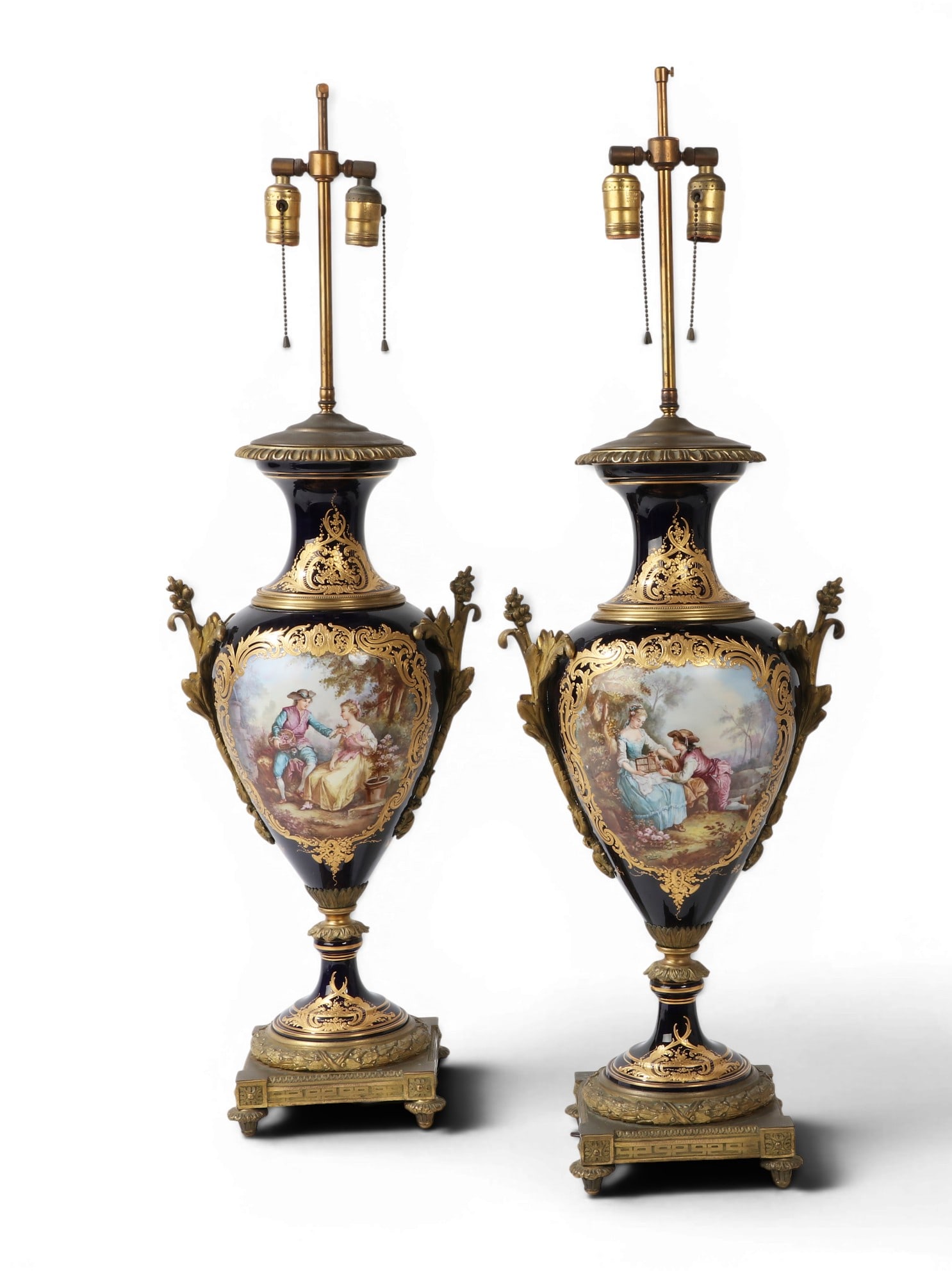 A pair of Sevres style gilt bronze mounted parcel gilt cobalt glazed porcelain urns as lamps: A pair of Sevres style gilt bronze mounted parcel gilt cobalt glazed porcelain urns now as table lamps 20th century Each with blue painted psuedo interlaced L enclosing E mark to underside. height ove