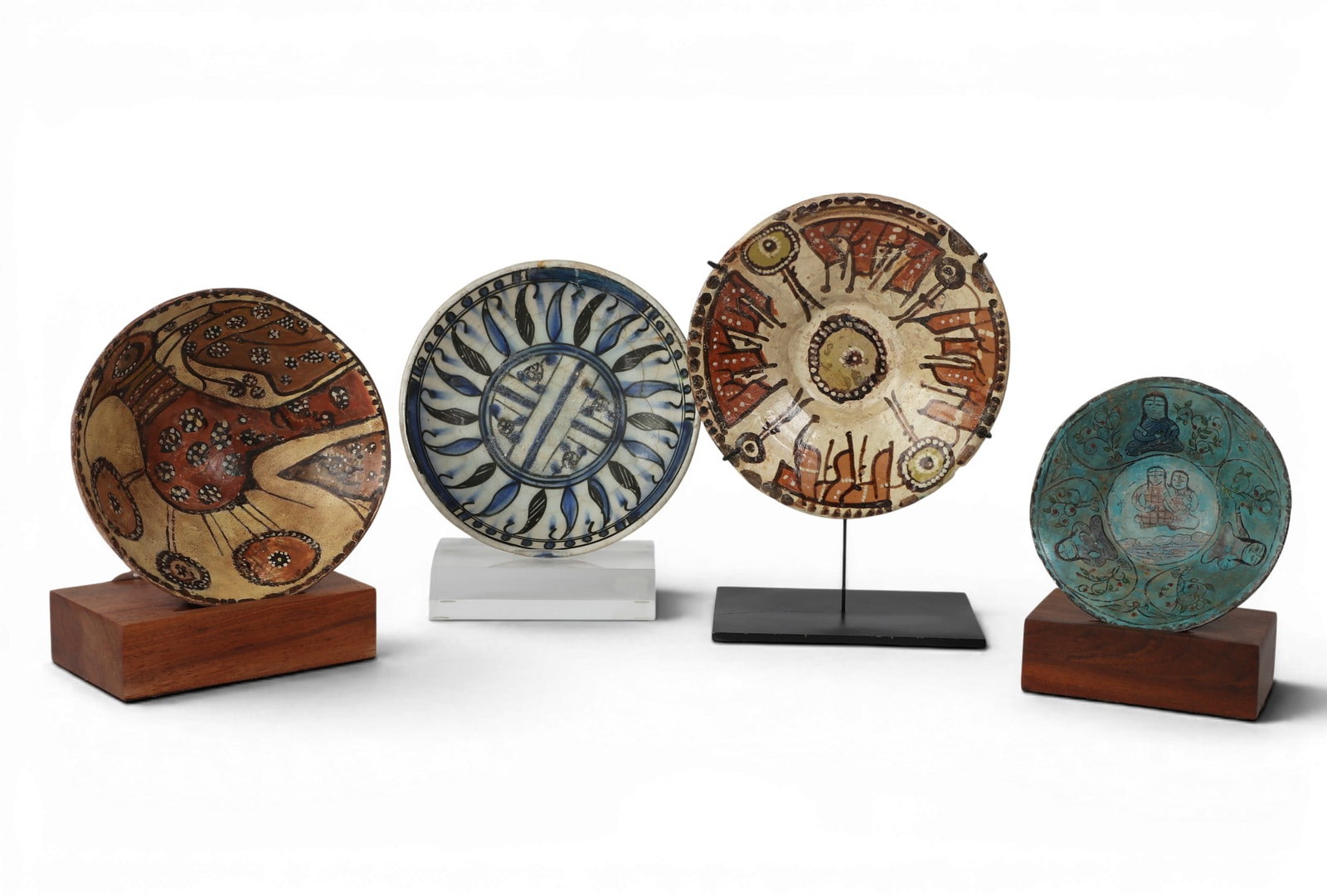 A group of four Persian polychrome glazed ceramic plates and bowls: A group of four Persian polychrome glazed ceramic plates and bowls Each on later stand. diameters ranging from 6 to 8 1/4in (15 to 21cm) Provenance: Property from the collection of Frederick M Nichola