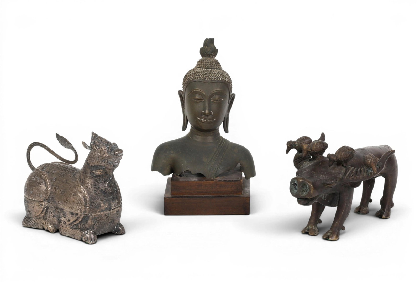 Three Asian metalwork table decoraions: Three Asian metalwork table decoraions Comprising a patinated bronze bust of a sukhothai Buddha on hard wood stand, a bronze model of a water buffalo with four oxpecker birds, a white metal betel nut 