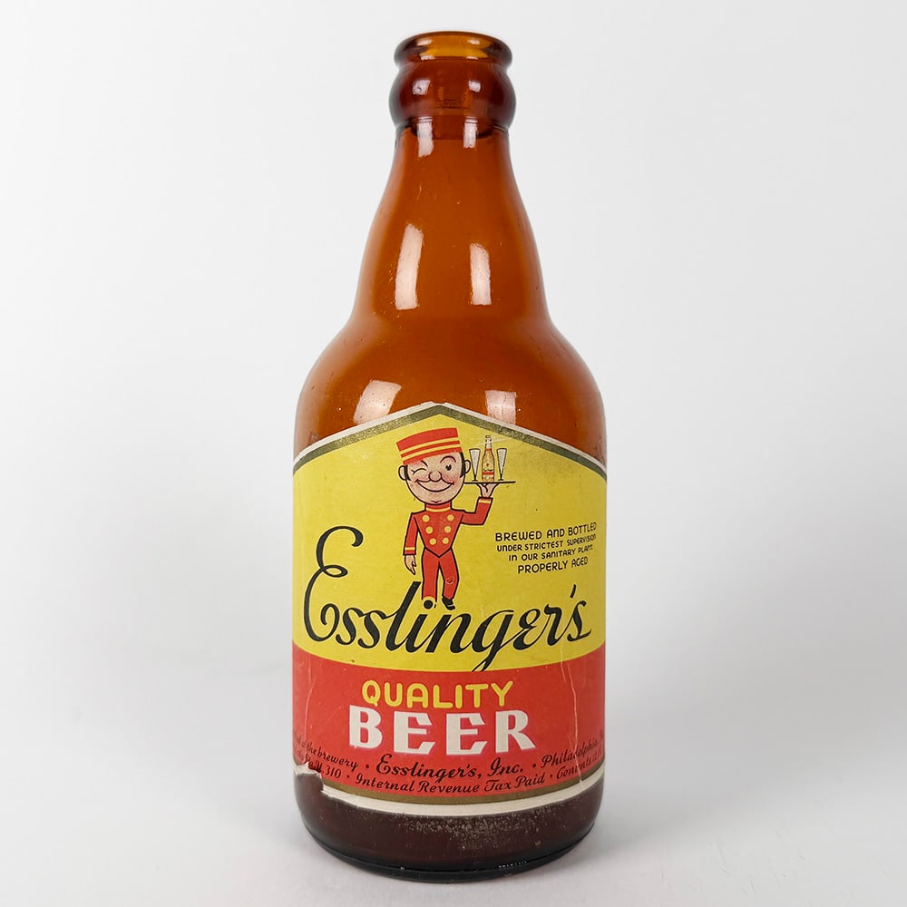 Esslinger's Quality Beer Steinie Bottle Philadelphia PA: Circa 1940s Esslinger's Quality Beer steinie bottle. Features a yellow and red label with a cartoon bellhop graphic. Esslinger's Inc., Philadelphia, Pennsylvania.