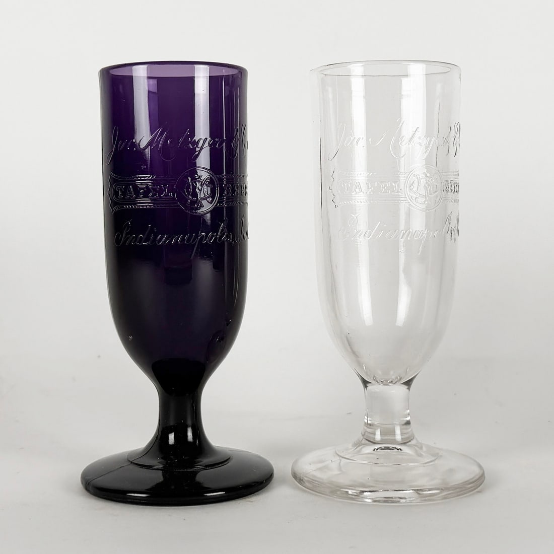 Indianapolis Brewing & Malting Co. Pre-Prohibition Glass Pair: Two footed glasses, one clear and one amethyst, with etched Indianapolis Brewing & Malting Co. logo and text. Early 20th century. One bid takes both.