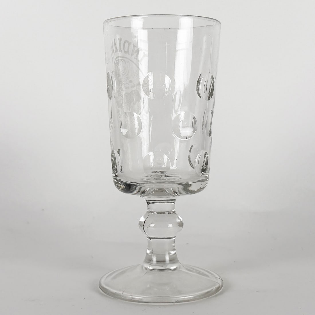 Indiana Brewing Association Pre-Prohibiton Goblet with Engraved Emblem: Pre-prohibition clear glass goblet featuring an engraved emblem and a pattern of circular indentations. Indianapolis Brewing Association. Indianapolis, Indiana. The goblet has a stemmed base and a cyl