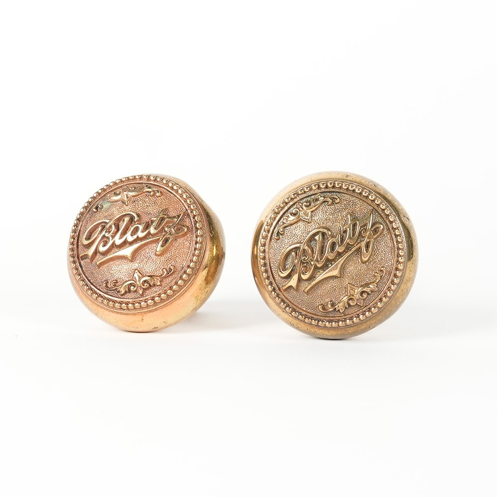 Blatz Brass Door Knob Pair OUTSTANDING: A portion of the proceeds from this lot will be donated to NABA. A pair of brass door knobs, each featuring the embossed name "Blatz" within a decorative border. One knob is shown detac
