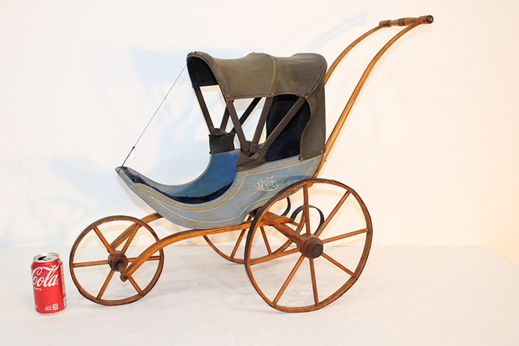19th C. 3 wheel Victorian doll carriage with oak frame and wheel. Label on the bottom says 1860 by: 19th C. 3 wheel Victorian doll carriage with oak frame and wheel. Label on the bottom says 1860 by Joe Ellis. 29" wide, 26" tall, 12" deep.