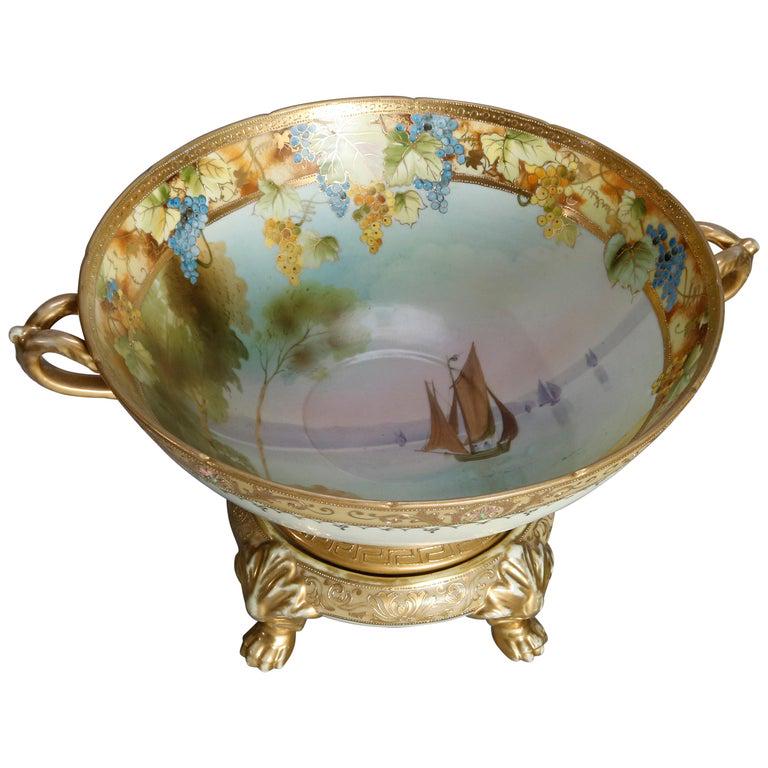 Japanese Nippon Painted & Gilt Seascape Bowl: An antique Japanese Nippon porcelain punch bowl offers hand painted bowl with seascape scene with sailing vessels bordered with grape and vine decoration, flanked by gilt scroll form handles and seate