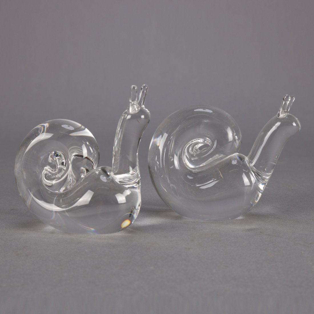 Pair Steuben Crystal Figural Snails: A pair of Steuben figural art glass snails, colorless, one signed and one unsigned, 20th century.Measures - 3"h x 3"w x 1"d; 3.25"h x 3.5"w x 1.75"d***IN-HOUSE SHIPPING & DELIVERY QUICK QUOTES AVAILAB