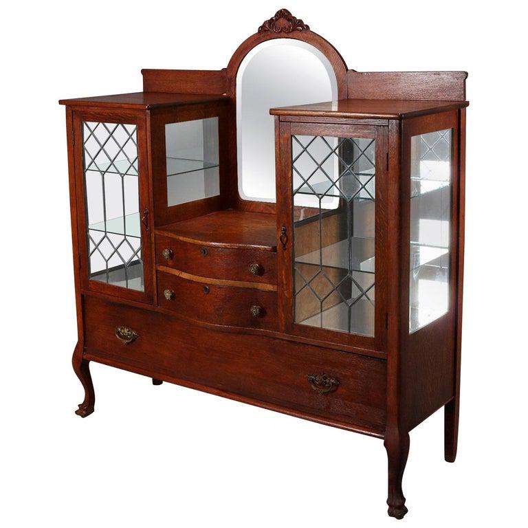 Antique Carved Oak Mirrored China Buffet, circa 1910: Antique China buffet features oak construction with central arched beveled mirror with carved foliate crest above two central drawers and having flanking enclosed glass china displays having glass sid