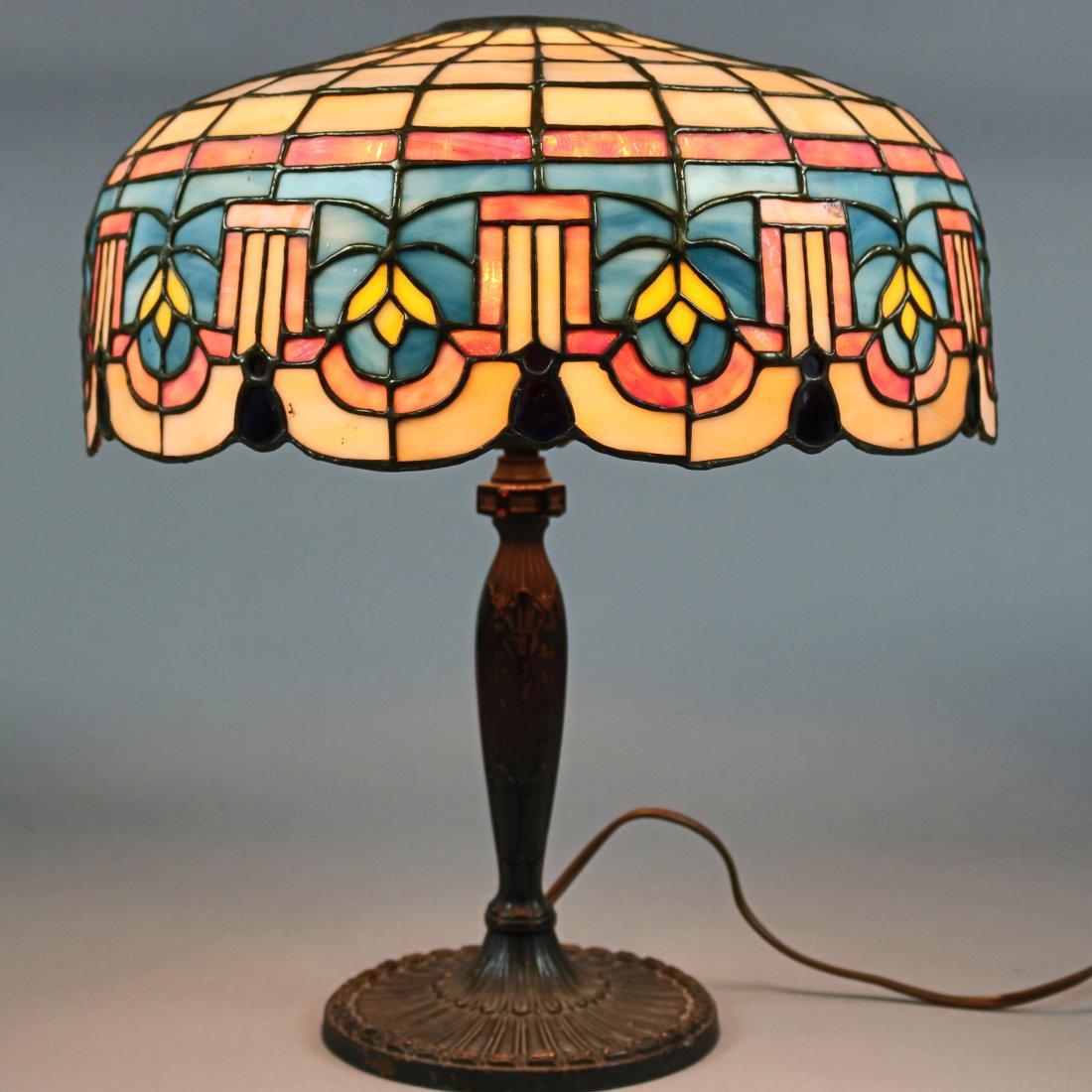 Antique Lamb Brothers Arts & Crafts Leaded Glass Lamp: An antique Arts & Crafts table lamp by Lamb Brothers offers domed leaded slag glass shade with stylized foliate and tassel decoration having scalloped edge and surmounting cast single socket base with