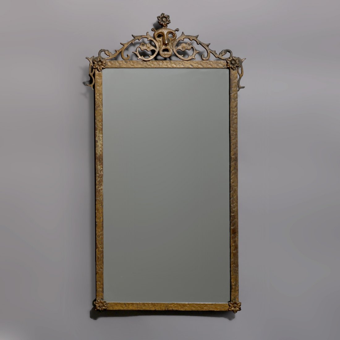 Oscar Bach School Gilt Metal Mask Mirror, c1920: An antique French Louis XIV wall mirror in the manner of Oscar Bach offers gilt cast metal frame with masquerade mask crest with flanking foliate elements and rosette at corners surmounting hammered f