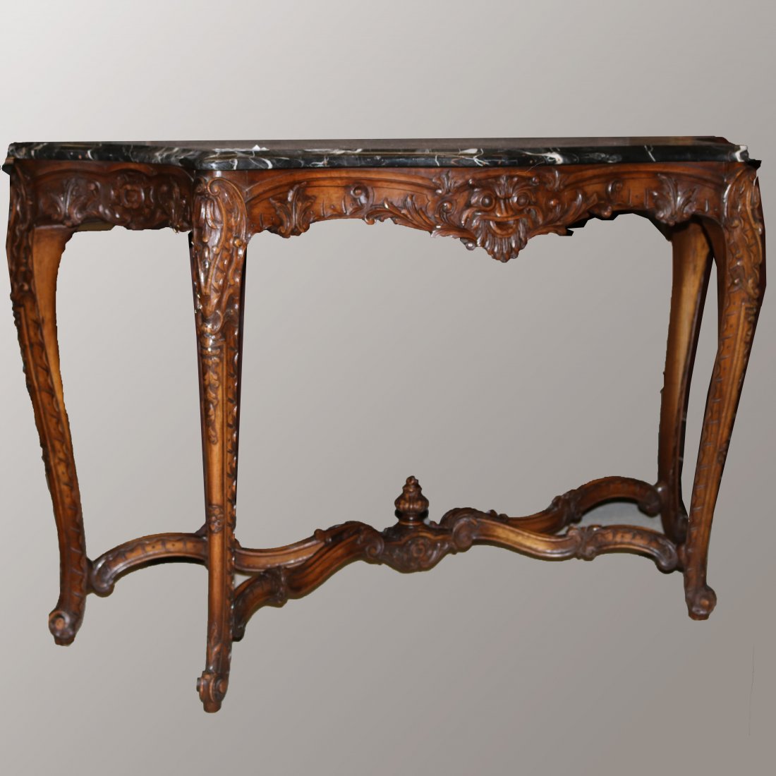 Antique Carved French Louis XV Marble Top Console Table: An antique French Louis console table offers shaped and beveled marble top surmounting foliate and shell carved base with cabriole legs with scroll form stretcher having central finial and seated on s