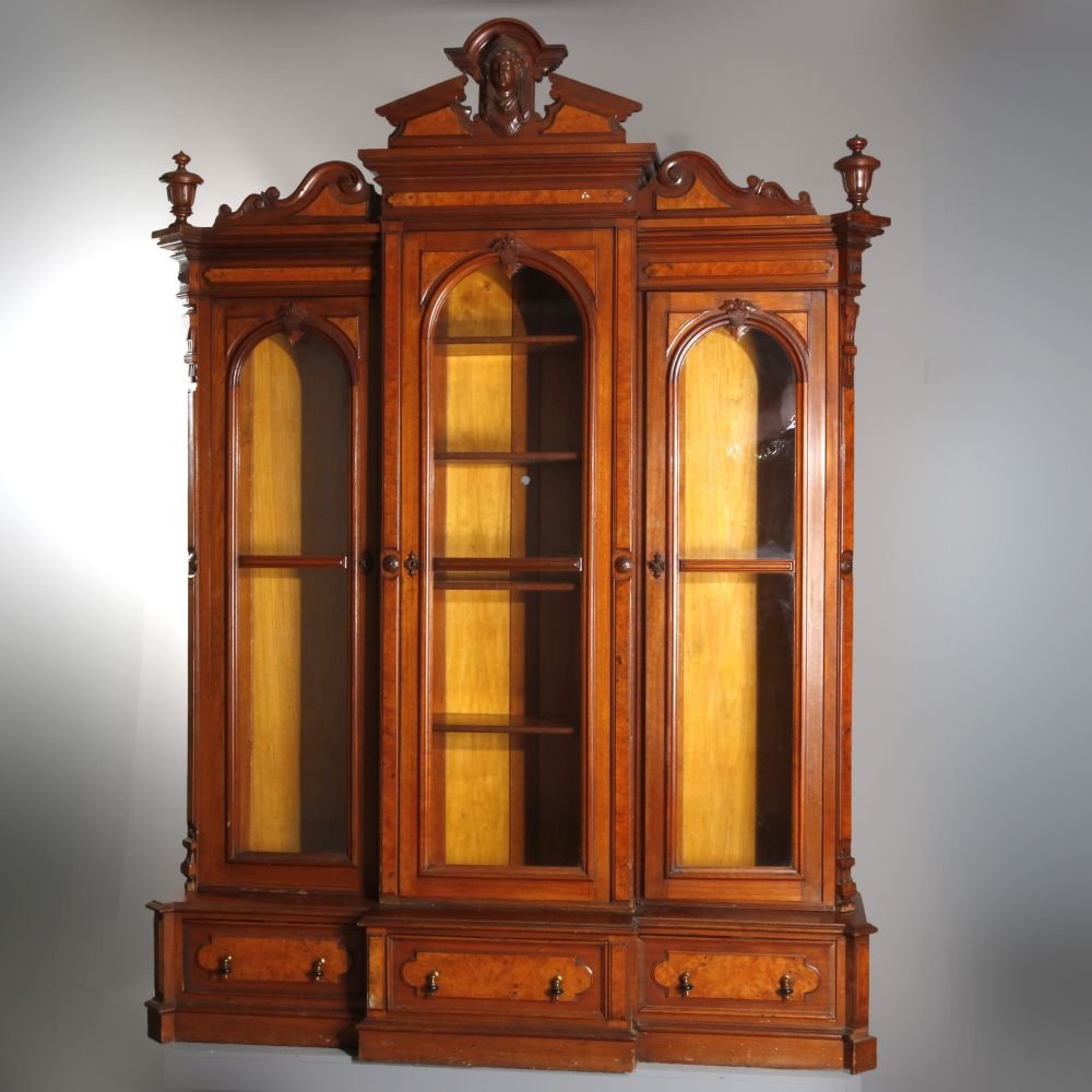 Antique Victorian Jelliff Figural Walnut, Burl Case: An antique oversized Victorian figural bookcase attributed to John Jelliff offers broken arch crest with carved Jenny Lind mask with flanking scroll and foliate elements bordered by urn form finials s