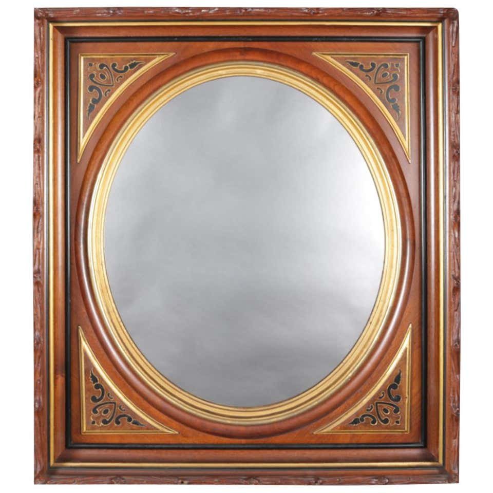 Carved, Ebonized and Gilt Deep Walnut Portrait Mirror: An antique deep walnut portrait wall mirror features frame with carved stick or branch form border and panelled cornices having ebonized and gilt scroll decoration, mirror framed by stepped gilt oval 