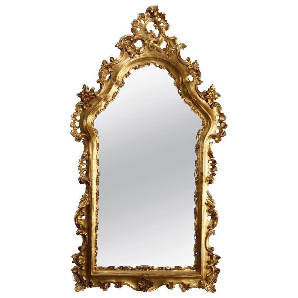Oversized French Rococo Style Giltwood Mantel Mirror: An oversized French Rococo wall mirror offers pierced giltwood frame with crest having central gadroon cartouche with flanking scroll and foliate elements surmounting shaped mirror, 20th century. Meas