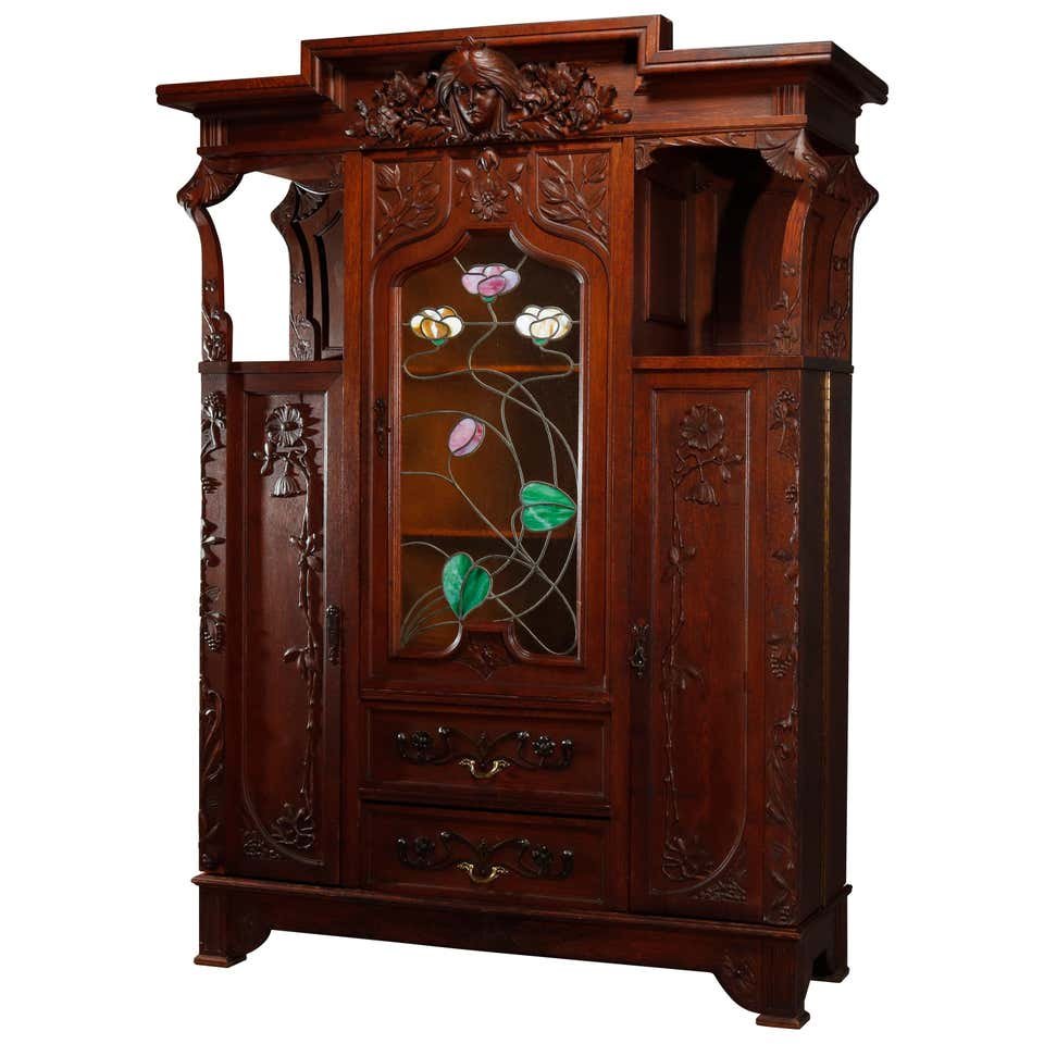 Art Nouveau Sarah Bernhardt Leaded Glass Bookcase: An antique Art Nouveau bookcase offers oak construction with crest having carved Alphonse Mucha style female mask of Sarah Bernhardt with flanking floral elements surmounting case with central cabinet