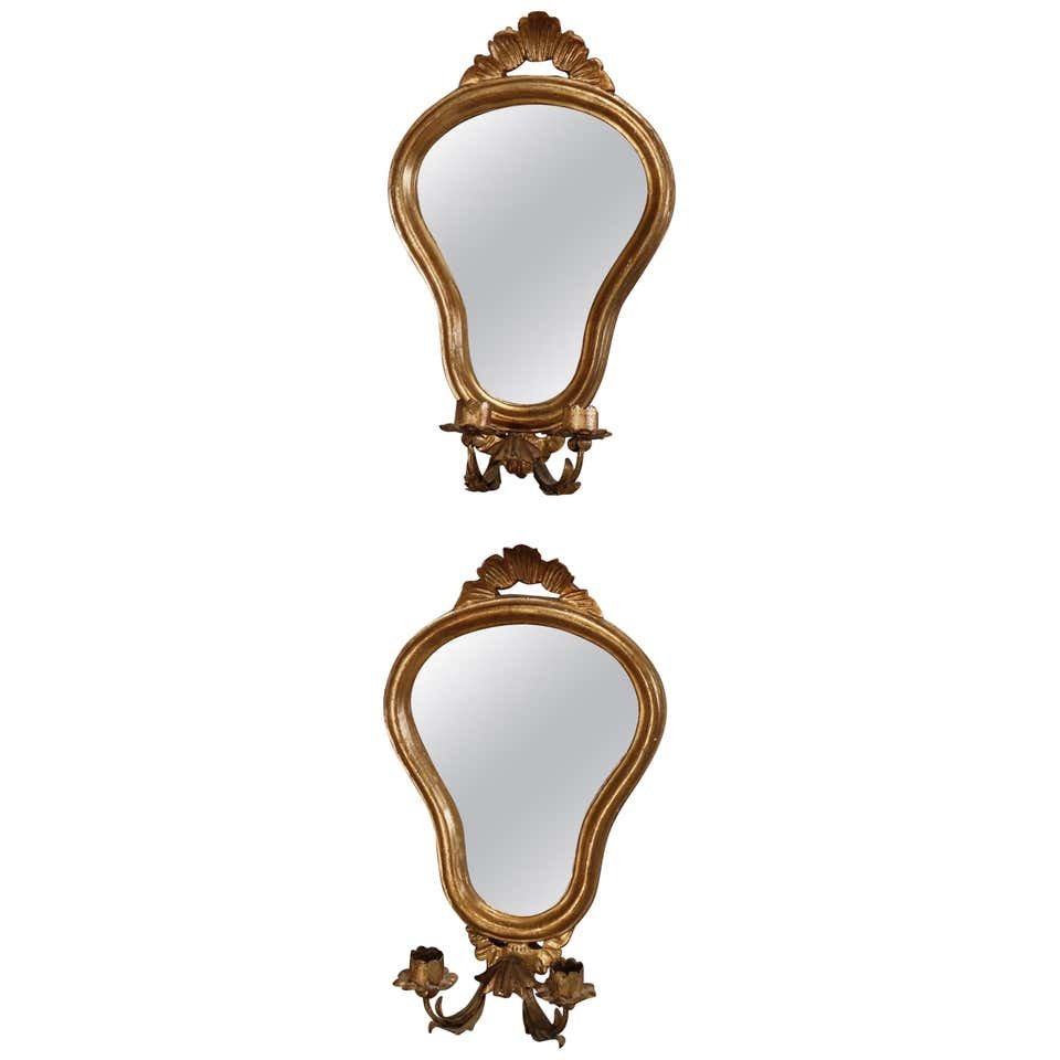 Venetian Style Mirrored Giltwood Candle Wall Sconces: A pair of vintage Venetian wall sconces offer giltwood frames in shield form with carved foliate cresta surmounting shaped mirror with two C-scroll foliate arms terminating in candle sockets, 20th cen