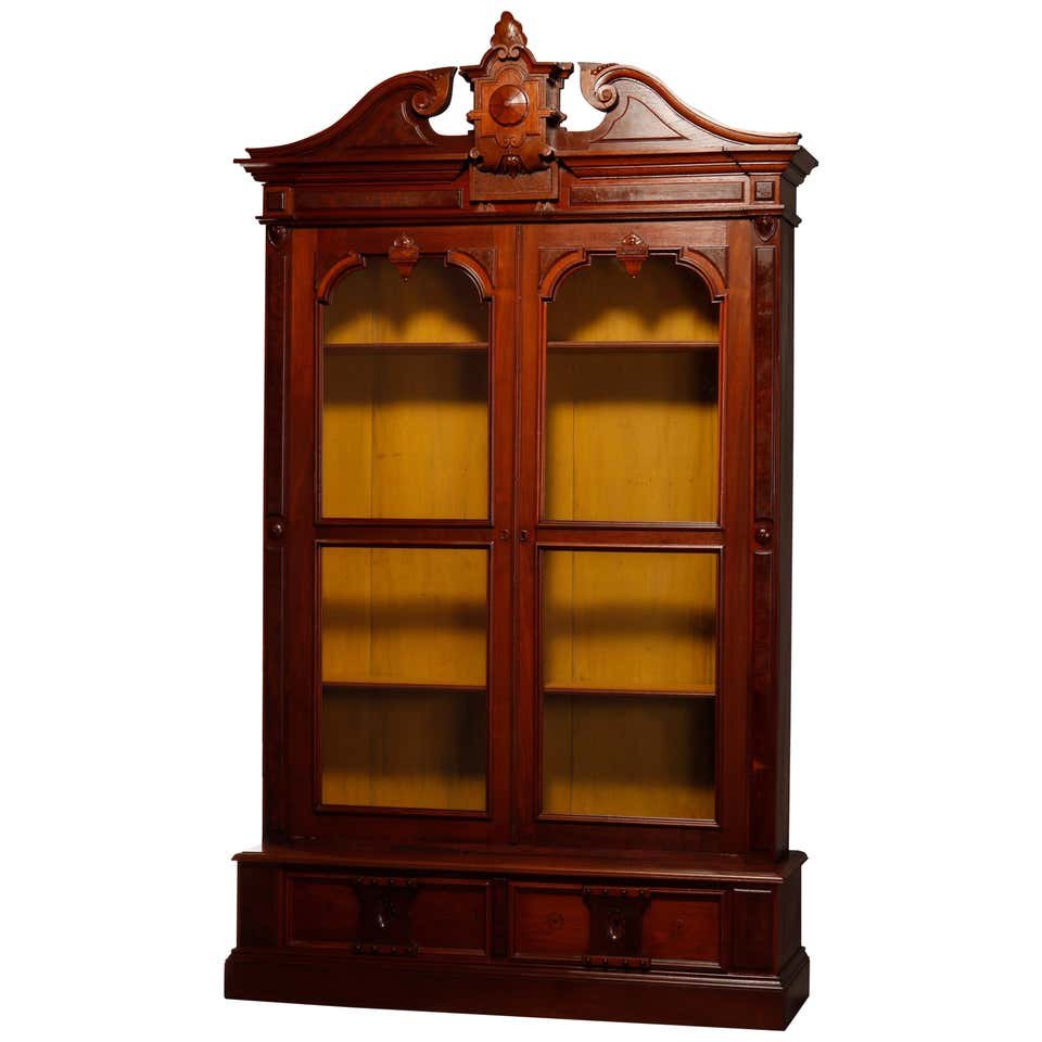 Oversized Renaissance Revival Carved Walnut Bookcase: An oversized antique Renaissance Revival bookcase offers walnut construction with caved broken arch crest having central stylized cartouche with scroll and foliate elements surmounting case with doubl
