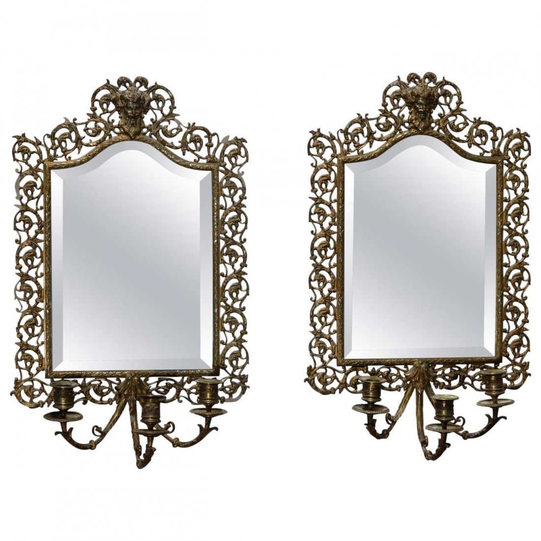 Oversized Figural Bronze Baroque Mirrored Candle Sconce: An antique pair of Baroque candelabra wall sconces offer cast scroll and foliate frame with central Wind God mask surmounting shaped and beveled mirrors with triple scroll arms terminating in candle s