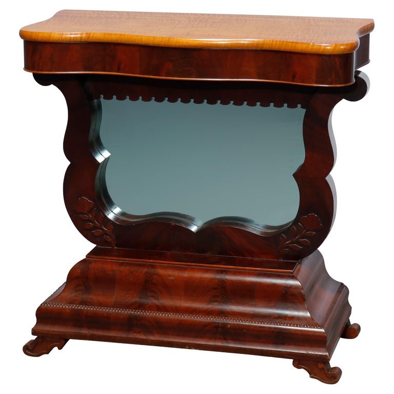 Antique American Empire Flame Mahogany Meeks School Pier Table, Circa 1840: An antique American Empire pier table in the manner of Joseph Meeks offers flame mahogany construction with shaped top surmounting lyre form base having carved floral decoration and central mirror, ra
