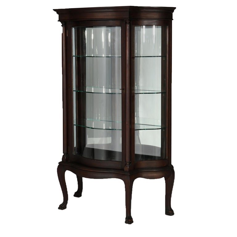 Antique Classical Mahogany Serpentine Paw Foot China Cabinet, circa 1900: An antique Classical vitrine offers mahogany construction in serpentine form with curved glass sides and single door opening to mirror back and shelved interior, raised on stylized cabriole legs termi