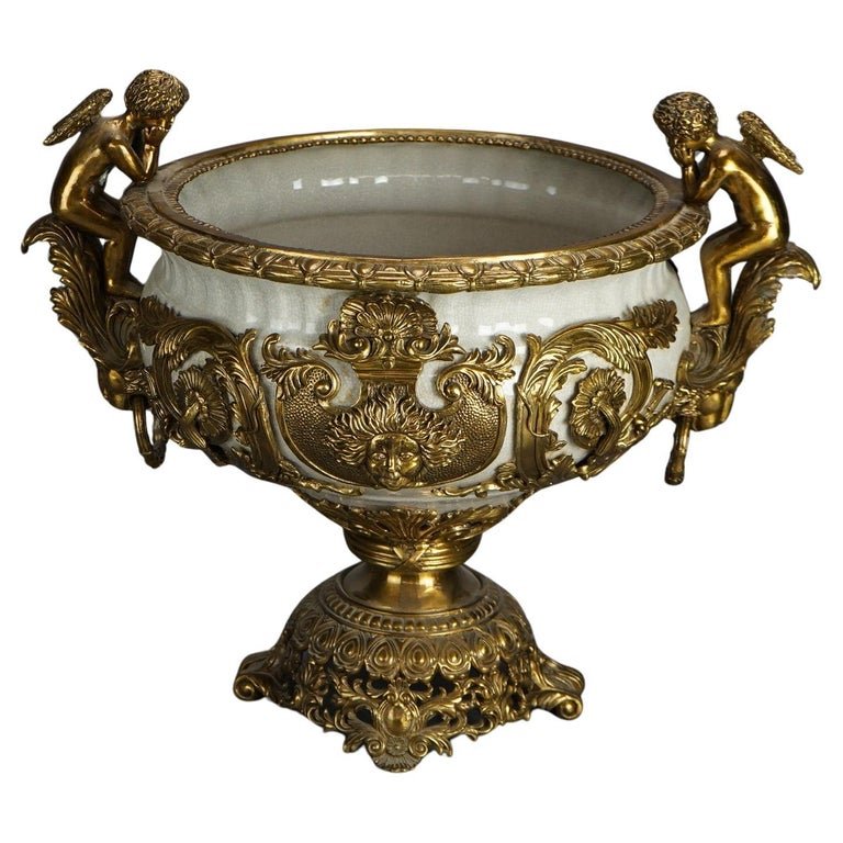 Oversized Neoclassical Gilt Bronze & Porcelain Rococo Figural Urn 20th C: A large Neoclassical Rococo style urn offers porcelain bowl with gilt cast bronze mounts including figural cherubi, floral and foliate elements, 20th century. Measures - 19.25"h x 22.5"w x 17"d. *** O
