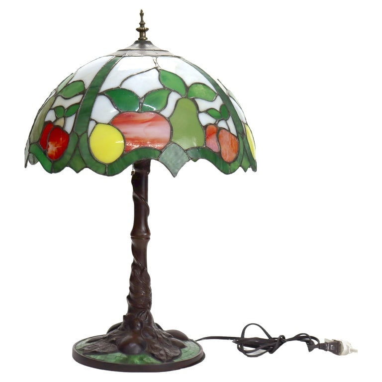 Arts & Crafts Leaded Stained Glass Table Lamp with Fruit Design 20thC: An Arts & Crafts table lamp featuring a leaded stained glass shade with a vibrant fruit motif. The lamp showcases a color palette including red, yellow, and green. The base is designed with an organic