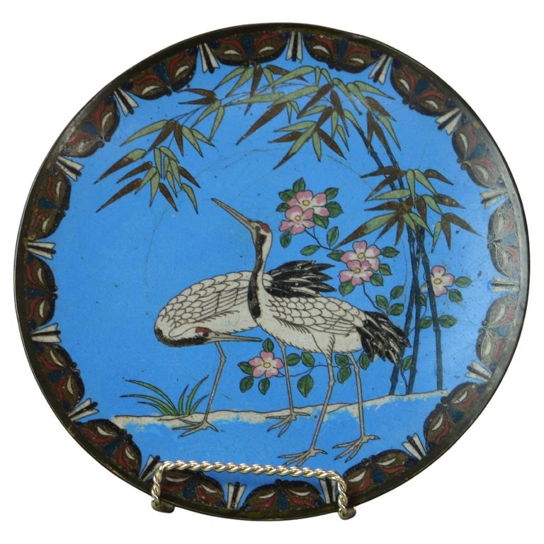 Antique Japanese Meiji Enameled Garden Scene Cloisonne Charger with Heron C1920: This cloisonné charger from the Meiji period features a beautifully enameled garden scene with a heron. The vibrant blue background highlights the intricate details of the heron, surrounded by bamboo