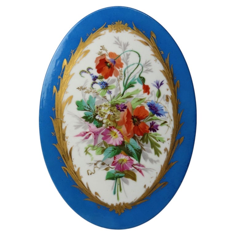 Sevres Style 11" Floral Painted Porcelain Plaque C1880: An antique Sevres style porcelain plaque from circa 1880, featuring a finely detailed floral painting. The plaque is oval-shaped with a vibrant blue border adorned with gold accents, framing a central