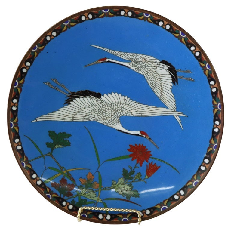 Antique Chinese Figural Bird Cloisonne Enameled Plate C1920: A finely crafted antique Chinese cloisonné plate from circa 1920, featuring an intricate design of figural birds, likely cranes, set against a vibrant blue background. The plate showcases traditional
