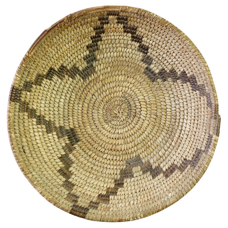 Southwest Navajo Decorated Low Basket C1920: A finely crafted Southwest Navajo low basket from circa 1920. This basket features traditional Navajo weaving techniques with a distinct geometric pattern. The natural fibers are woven tightly, showca