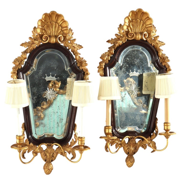 Pair 30" English Regency Carved Mahogany & Gilt Wood Mirrored 2-Light Wall Sconces C1840: This pair of antique English Regency mirrored sconces, dating to approximately 1840, exemplifies the opulent aesthetic of the early Victorian era with strong Georgian influences. Crafted from richly c