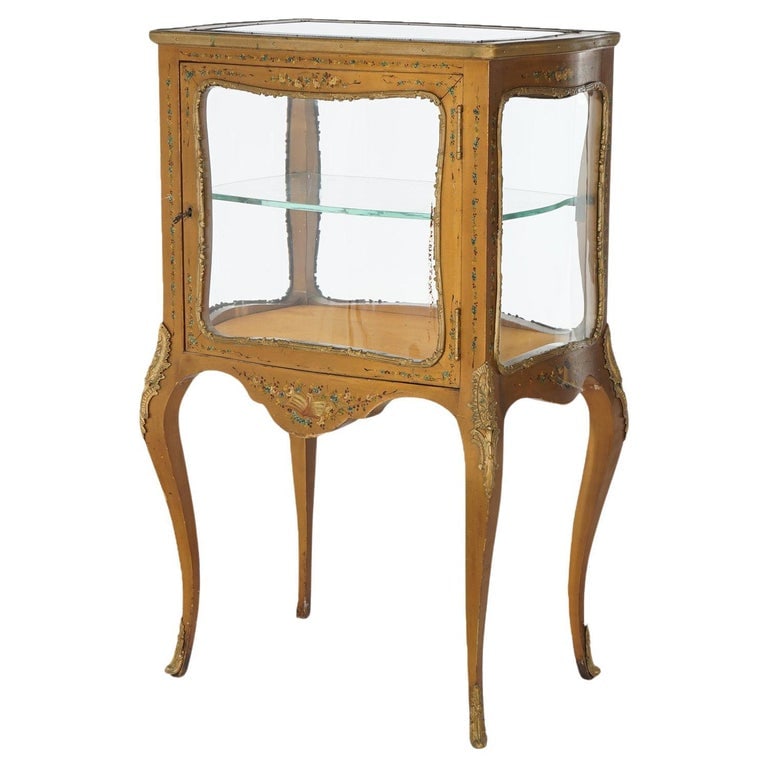 French Louis XV Style Giltwood Vitrine W/Hand Painted Floral Elements C1910: This antique French vitrine, crafted in the Louis XV style, dates to circa 1910. It features a beautifully giltwood frame adorned with intricate hand-painted floral motifs. The vitrine stands on elega