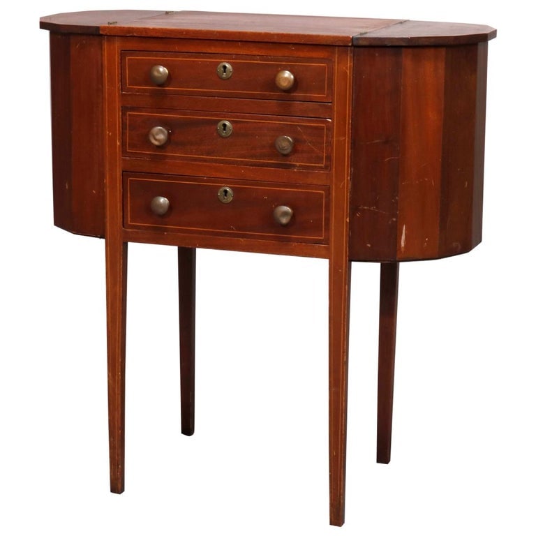 Martha Washington Mahogany Sewing Stand with Project Pockets C1930: An antique Martha Washington sewing stand or cabinet offers mahogany construction with central tower having graduated drawers and flanked by faceted demilune project pockets, raised on tapered satinwo