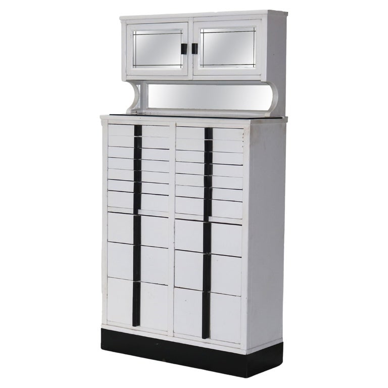 Art Deco Dental Cabinet with Mirror C1920: A fine example of Art Deco design, this antique dental cabinet from circa 1920 features a sleek white finish with black accents. The cabinet includes multiple drawers for storage and a mirrored upper 