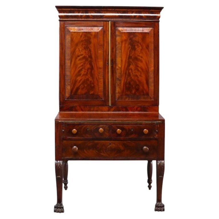 American Empire Classical Flame Mahogany Clawfoot Secretary Desk C1840: An antique American Empire Classical secretary desk, crafted circa 1840. This desk is constructed from flame mahogany, showcasing a rich, swirling grain pattern. The upper section features a cabinet w