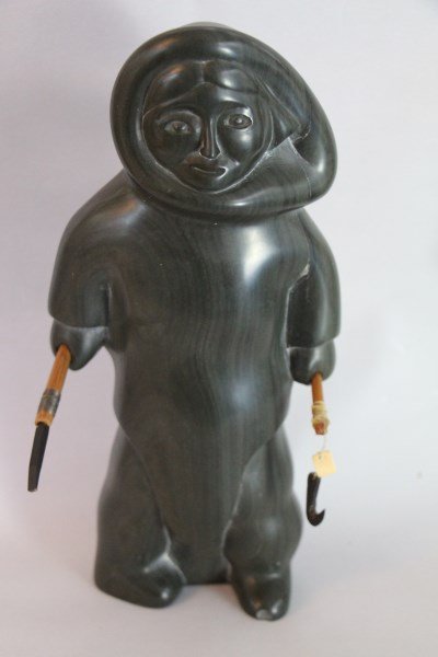 INUIT STONE CARVING - ALLIE APPAQAQ: (1915-1986) FISHERWOMAN WITH ICE CHISEL AND JIGGER. CIRCA EARLY 1970'S. DARK GREENSTONE, BALEEN, IVORY AND SINEW, SIGNED IN SYLLABICS, small chip to front of left foot 11.5" H