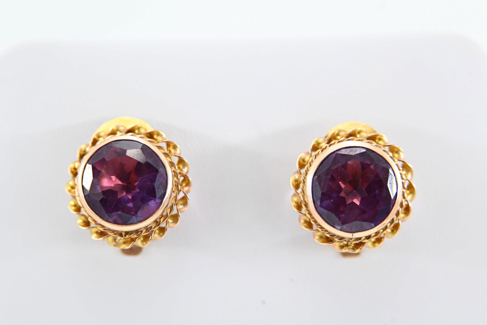 Pair of Vintage Rose Gold Amethyst Pierced Clip Back Earrings: A pair of vintage 14K rose gold amethyst earrings with decorative rope and ribbon borders. Key Features: 14K rose gold Each earring bezel set with a round faceted amethyst, approx. 4.5 carats Rope and