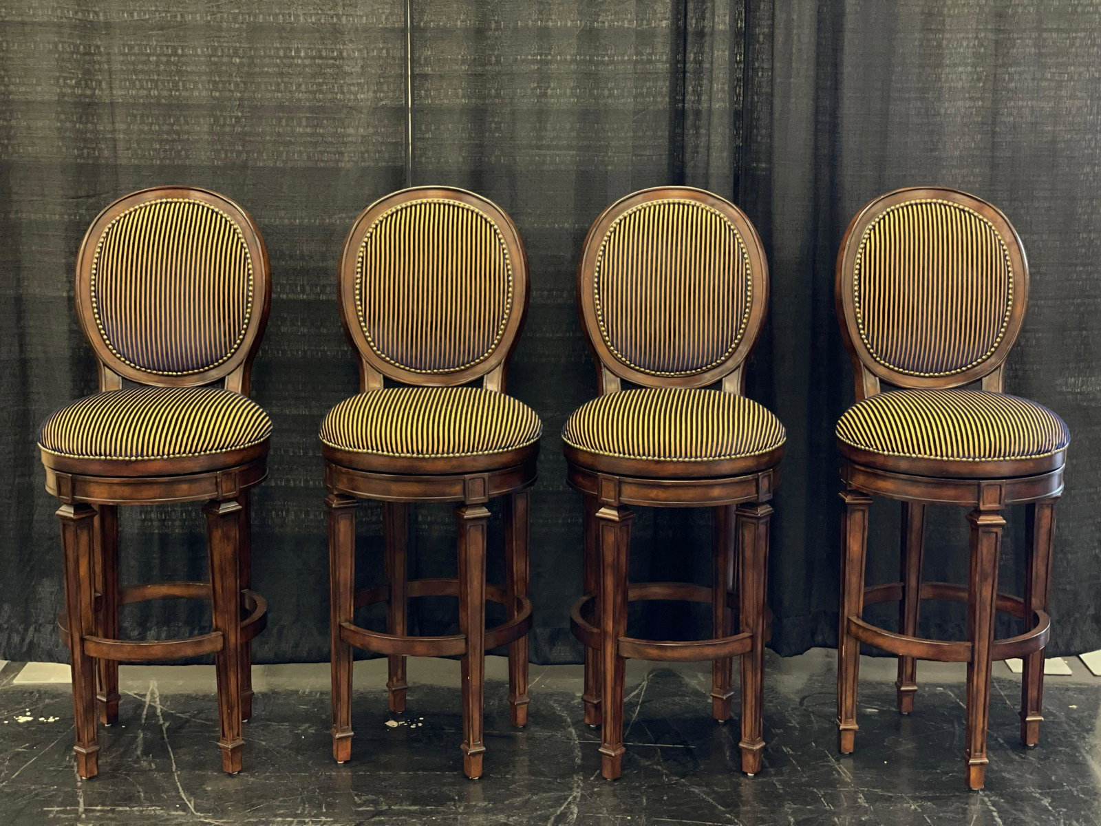 4 Hillsdale Furniture Upholstered Swivel Bar Stools: Lot of 4 swivel top bar stools by Hillsdale Furniture. They feature a gold and blue upholstered seat and back along with studded accents. They measure approximately 49” x 19.5”. Seat heigh
