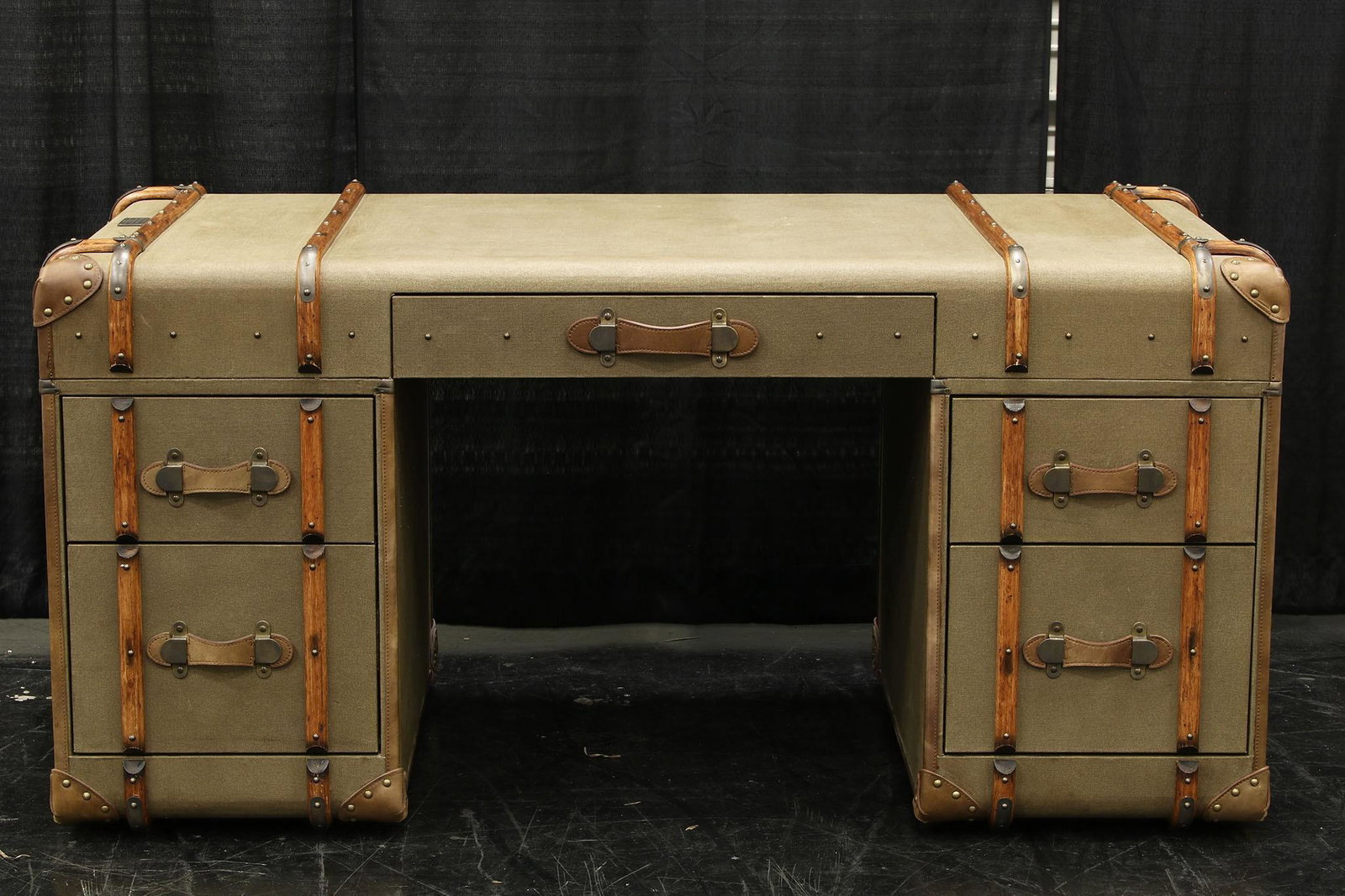 Tom Richards Antique Travel Trunk Desk: A Tom Richards travel trunk desk in army green with wood banding and leather strap handles. Measures approx 30.5” h x 64” w x 33” d. Desk shows some wear here and there consistent wi