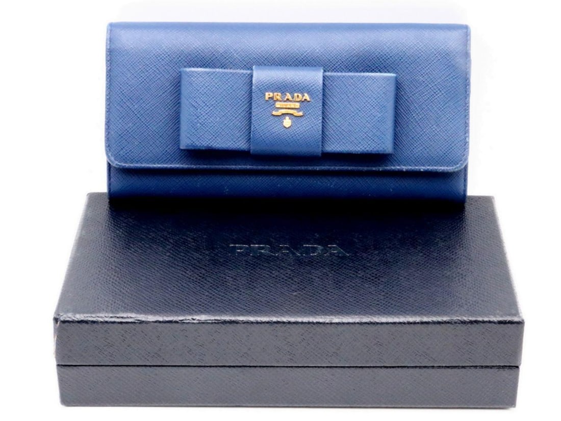 Prada Saffiano Leather Bow Wallet: PRADA, A SAFFIANO LEATHER BOW WALLET Fashioned in Prada’s signature Saffiano leather, this Bow wallet features a charming front bow detail that softens the structured, minimal silhouette. The co