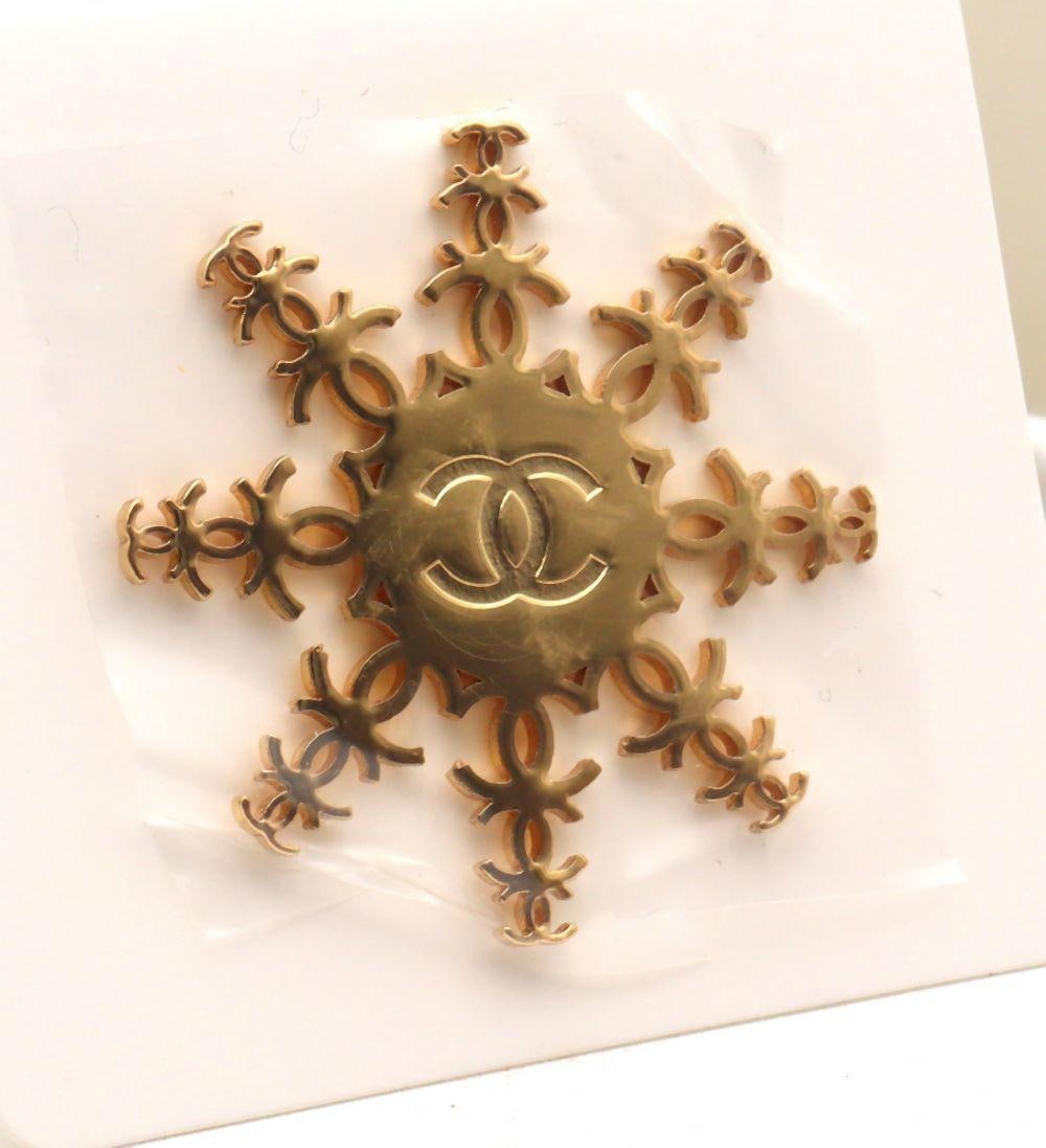 Chanel Beaute "Snowflake" Brooch: Chanel Beauté Snowflake Brooch. Featuring a gold-tone snowflake design. Includes the original "With Compliments of Chanel Beauté" packaging. Measures approx. - 1 1/2" Dia. Condit