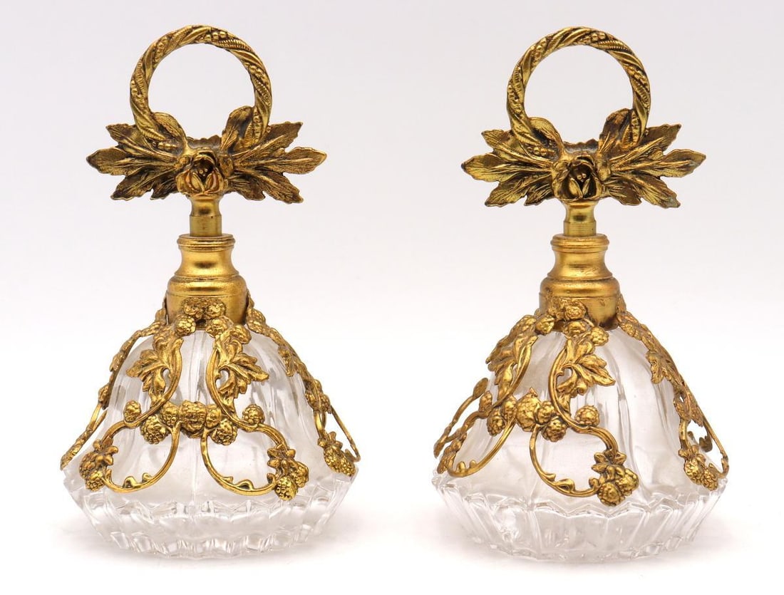 19th C. Cut Glass and Brass Perfume Bottles, Group of 2: Unmarked Perfume Bottles, Group of 2 Cut glass with brass overlay, unsigned Each: 5" H x 3" Dia. Condition: Good condition with loose brass overlay and a stuck stopper to one bottle. Have a