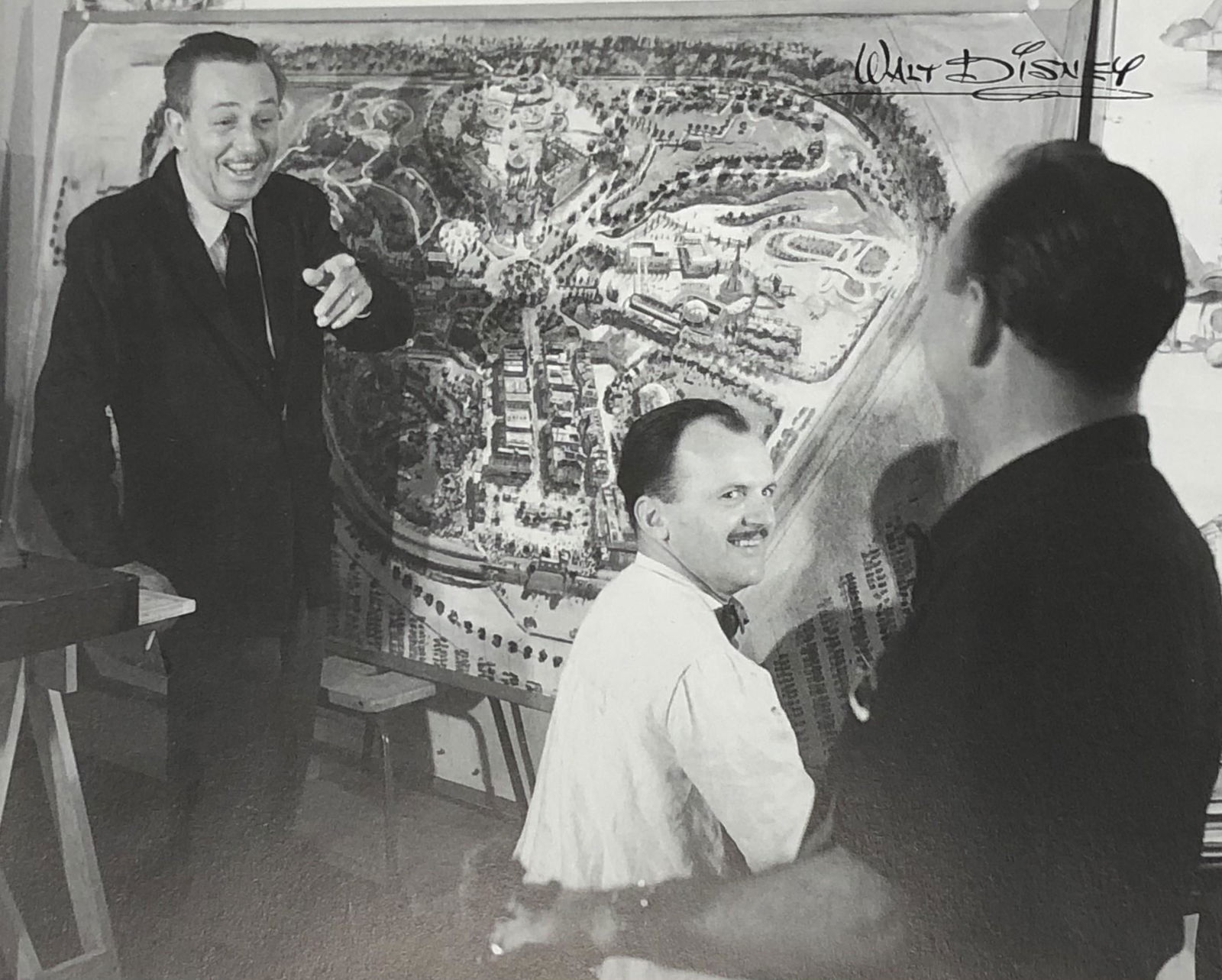 Photo-Litho of Walt Disney (Aerial Map of Disneyland): Photo-Litho of Walt Disney with Peter Ellenshaw and his aerial map of Disneyland, 1954 Printed circa late 20th c. 7 5/8" x 9 5/8" Stamped to top right side "Walt Disney"