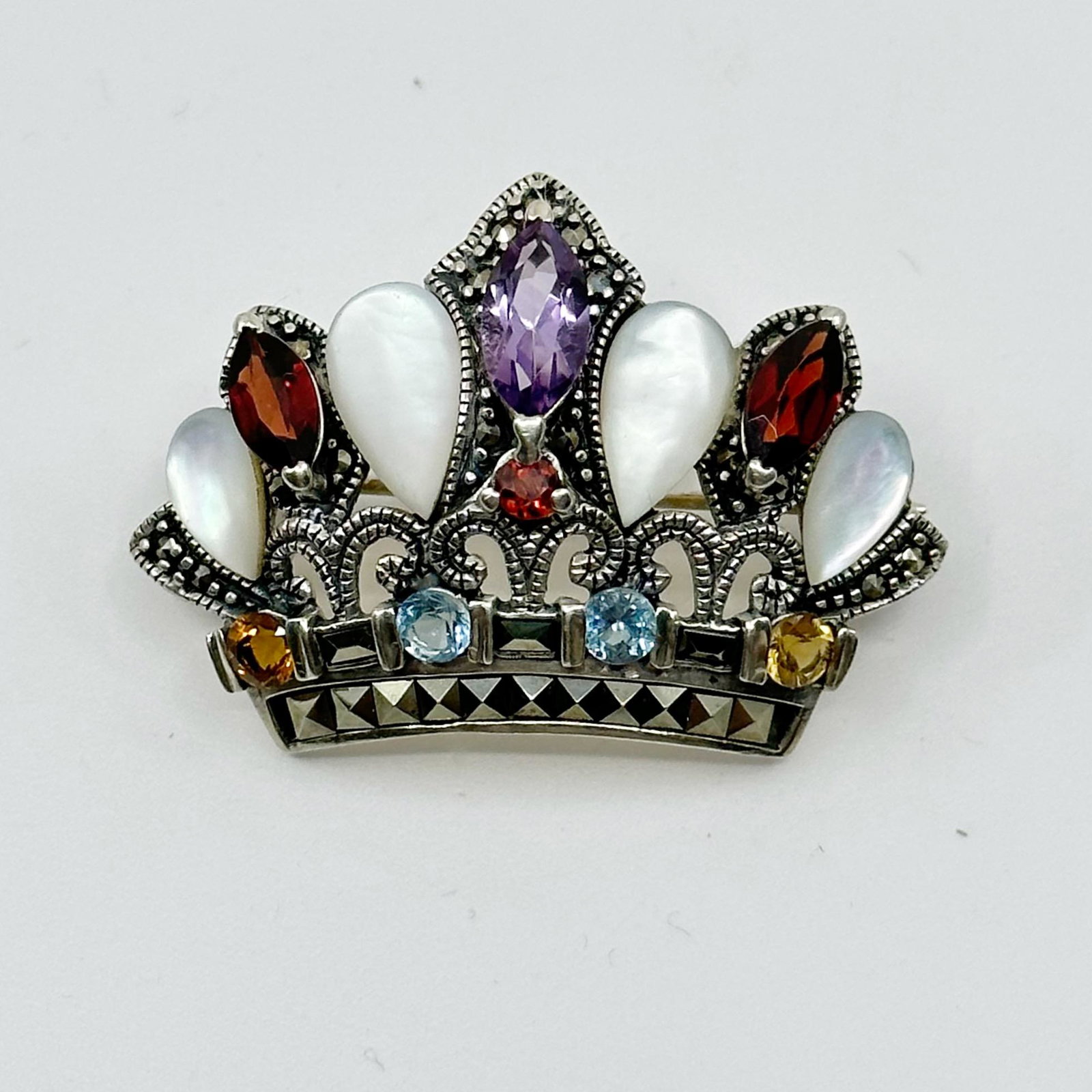 Sterling silver gemstone & marcasite crown Brooch: Measures: 1" long by 1 1/2" wide Crafted with garnet, amethyst, citrine, blue topaz & marcasite Signed: A 925 In very good condition SKU-890