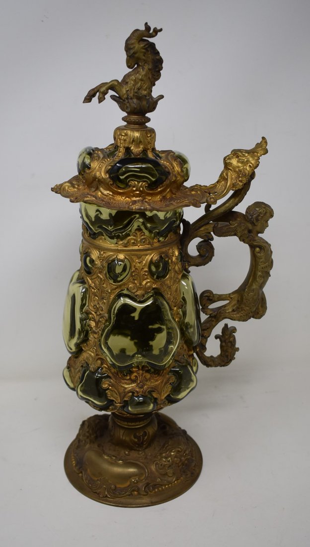 Green Glass & Figural Metal 1 Liter Beer Stein: Green Glass & metal 1 Liter Stein Dated 1899 with Figural Goat on the Lid, winged soldier on handle, and a lion amongst other motifs. Incredible Metalwork w/ Glass body blown in filling the openings i