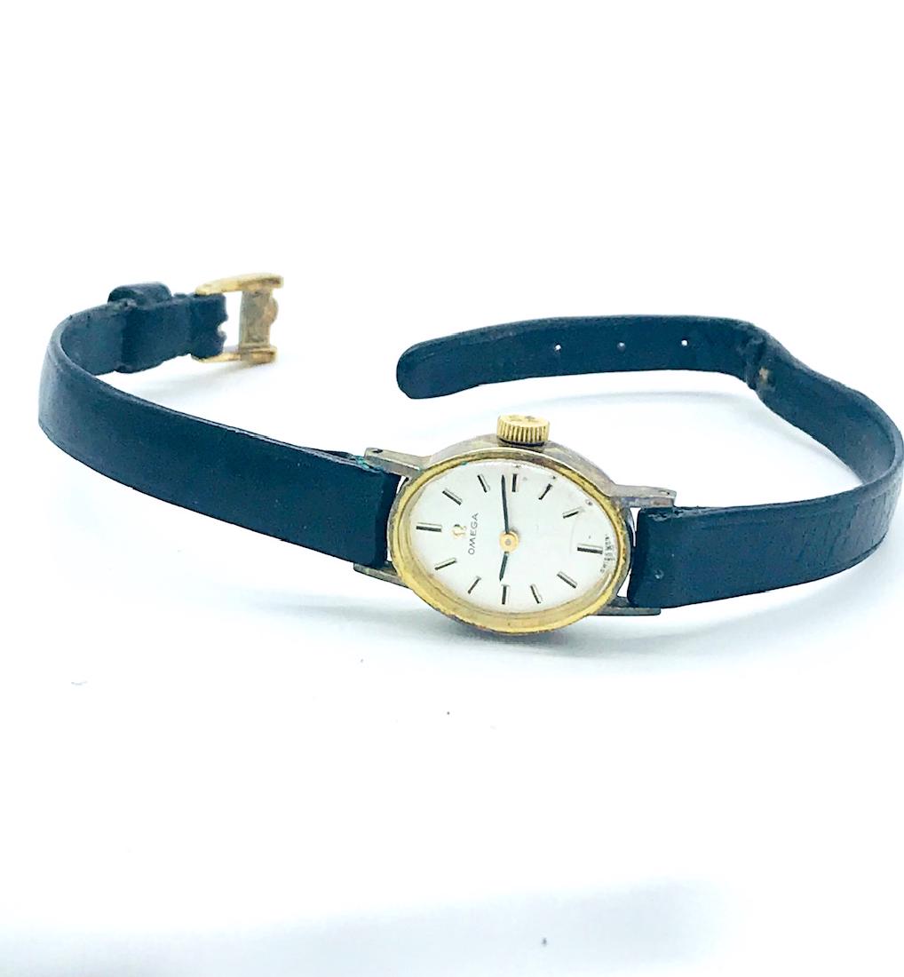 1970's, Omega Ladies Manual Wind Watch: 1970's, Omega Ladies Manual Wind Watch 1 inch length face of watch, gold framed case, white dial with stick markers, original black strap GIA Gemologist inspected and evaluated